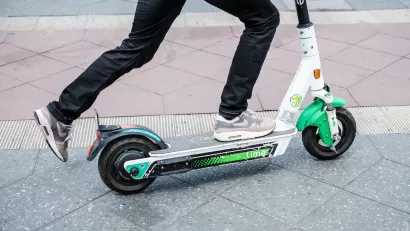 Close-up of person riding green and white Lime e-scooter.