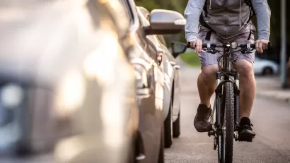 Man on bike rides next to parked cars.