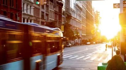Blurred image of New York City bus driving through intersection with 5th Avenue with golden hour sunset sky in background.
