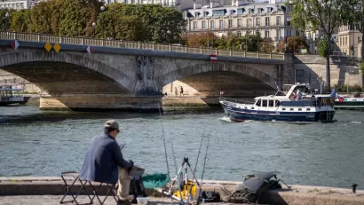 Man sitting in chair along River Seine in Paris with fishing pole.