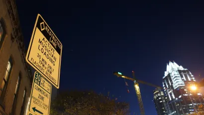 Close-up of musicians loading zone sign on Sixth Street in Austin, Texas at night with illuminated high-rise with pyramidal top in background.