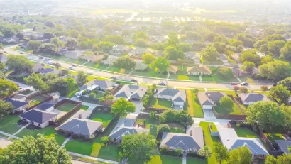 Aerial view of suburb outside Dallas, Texas with large single-family houses with enclosed backyards and green lawns.