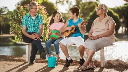 Grandparents sitting on bench with young girl and boy, girl holding ball and boy holding ukelele.