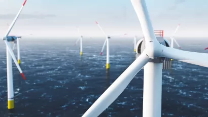 Close-up of top of white offshore wind turbine with other turbines in sea in background.