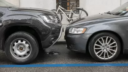 Two grey cars parked nose to nose, one taller than the other, on city curb with parked bicycle visible on sidewalk.