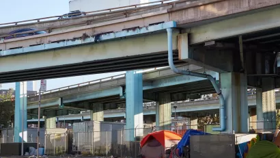 Tents set up against fence by unhoused people under freeway overpass in San Francisco, California.