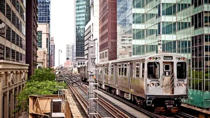 Silver Chicago train passing by dense high-rise buildings on elevated track.
