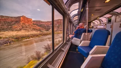 Amtrak train with large curved windows passing through scenic Rocky Mountain red rock canyon
