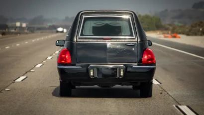 Black hearse seen from behind driving on multilane road.