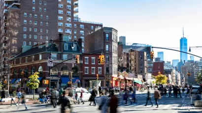 Street scene in Greenwich Village, New York City with people walking through busy intersection and new WTC tower in background.