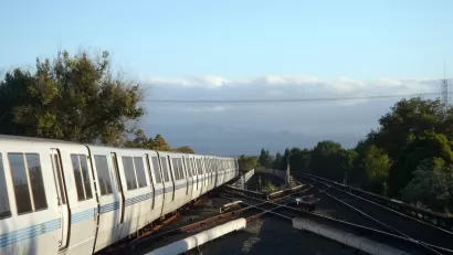 BART heavy rail train on elevated track pulling into Concord, CA station with cloudy sky and trees in background.