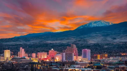 Skyline of Reno, Nevada against snowy mountains and bright red sunset sky.