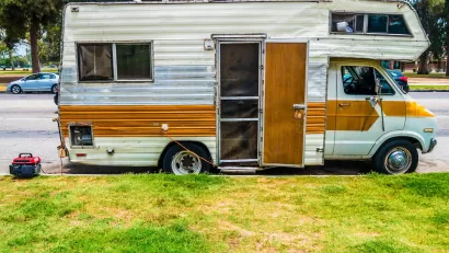 Old white motor home with brown stripe and open door parked on street in Los Angeles, California.