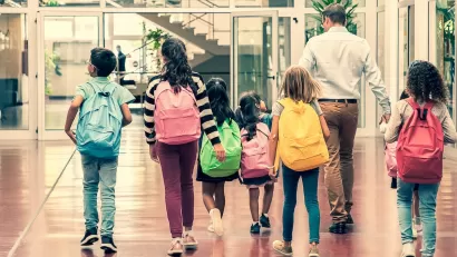 Back view of group of six children and one adult walking down school hallway.