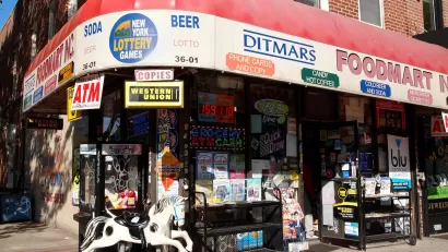 Corner convenience store with red awning and children's rocking horse toy out front in brick building in Queens, New York City