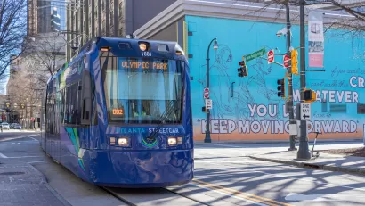 Blue Atlanta Streetcar to Olympic Park on street in downtown Atlanta with colorful mural on building in background.