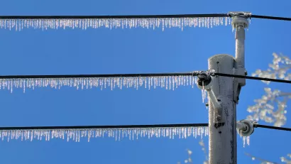 Power lines with dense icicles hanging from them against blue sky.