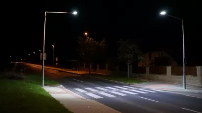 Empty street with crosswalk lit by two tall street lights at night.