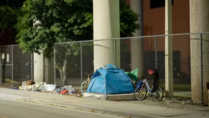 Tent occupied by unhoused resident with bike against fence under underpass in Miami, Florida.
