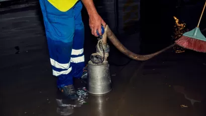 Worker in blue pants holding hose while standing in flooded interior room.