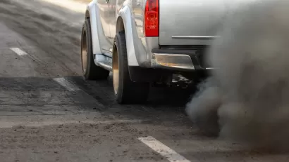 Close-up of driver's side of silver truck with cloud of dirty emissions from tailpipe.