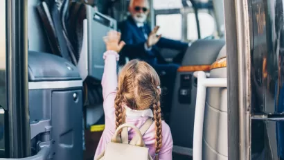 Young girl with pigtail braids boarding bus with blurred bus driver in driver's seat in background