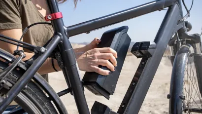 Close-up of person changing battery on black electric bike outdoors.