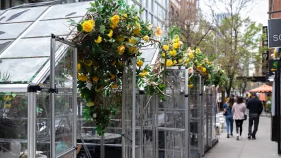 Transparent glass outdoor dining pods with yellow flowers on a sidewalk in New York City during the Covid-19 pandemic.