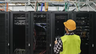 Worker in yellow safety vest and hard hat looks up at servers in data center.