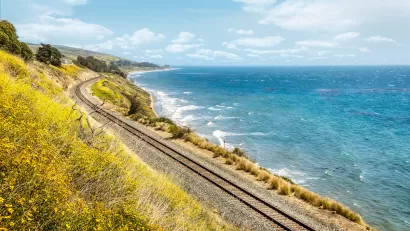 Train tracks along California coast with yellow wildflowers blooming on one side and blue Pacific Ocean on the other.