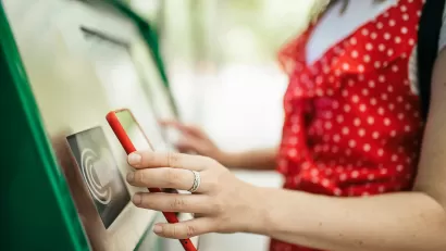 Close-up of woman holding up smartphone up to contactless public transit payment kiosk