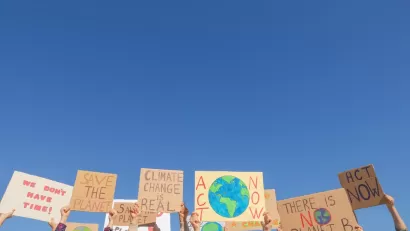 Hands holding up climate change protest signs against blue sky.
