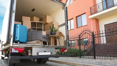 Moving truck with open back door with furniture and a blue suitcase visible inside.