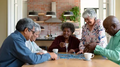 Group of older people sitting at table indoors laughing.
