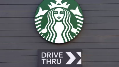 Close-up of Starbucks coffee logo with Drive Thru sign with arrow under it mounted on dark grey wall.