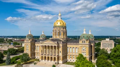 Ornate, tan stone capitol building with a gold dome roof and low-rise city buildings in the background.