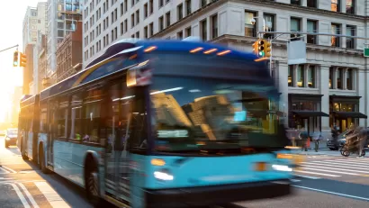 Blue and green city bus blurred in transit on New York City street.