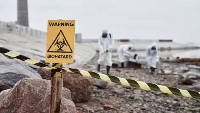 Close-up of yellow "Warning Biohazard" sign with people in hazmat suits cleaning up in background.
