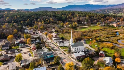 Aerial view of Stowe, Vermont, small rural town with tall church steeple and forest and mountains in background.