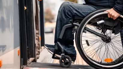 Close-up of person in wheelchair wearing jeans entering public bus on ramp.