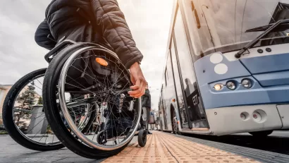 Ground-up view of man using wheelchair waiting to board a light blue bus.