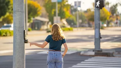Woman pressing beg button at crosswalk about to cross street.