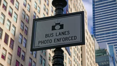 Close-up of "Bus Lanes - Photo Enforced" sign with camera logo on New York City street pole.