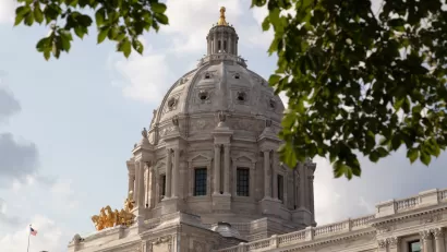 View of Minnesota state capitol dome from side with leafy tree branches slightly obscuring view.