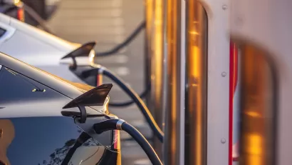 Close-up of row of electric cars plugged into chargers at outdoor station.