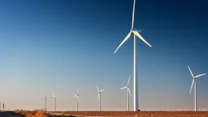 Row of white wind turbines in wide open dirt field in west Texas.