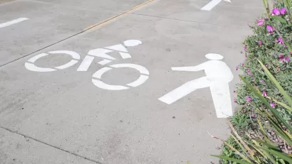 Close-up of white pedestrian and bike symbols painted on concrete path.