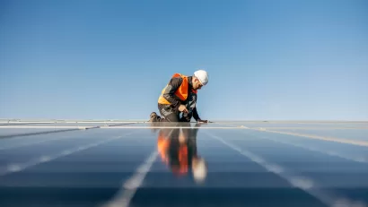 Worker in safety vest and white hard hat installing rooftop solar panel.