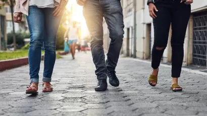 Close-up of bottom half of three people walking down city sidewalk paved with paving stones.