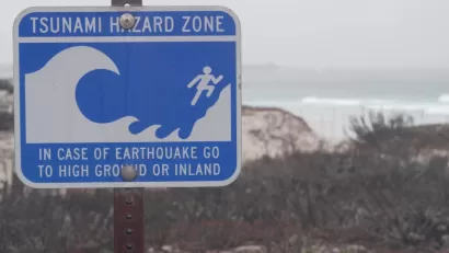 Close-up of blue and white tsunami warning sign on coast in Monterey, California on gloomy day.